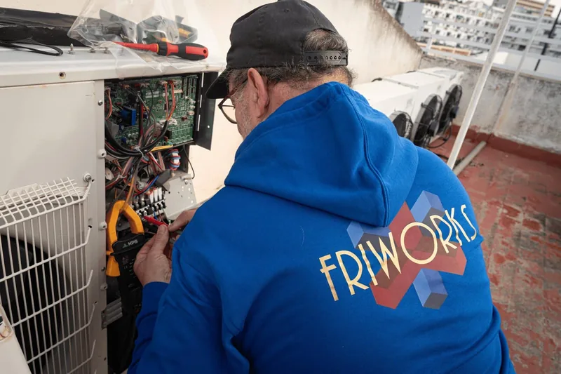 Técnico de Friworks midiendo con una pinza amperimétrica en el cuadro eléctrico de una unidad exterior de climatización
